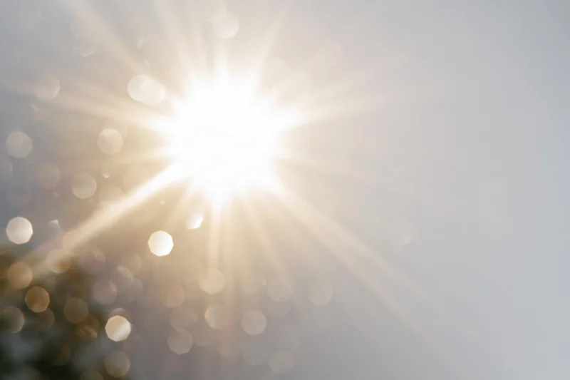Intense sun flare bursting from center-left against bright sky with bokeh highlights