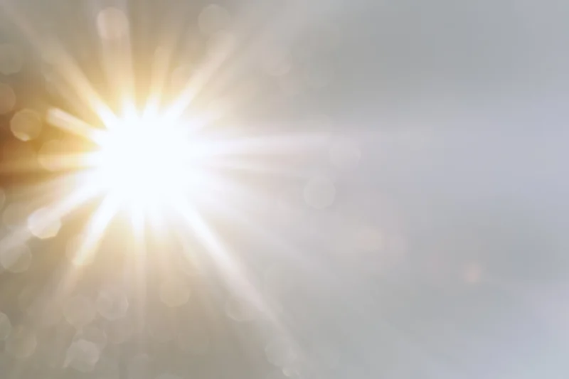 Intense sun flare bursting from center-left with soft bokeh and bright rays across a light background
