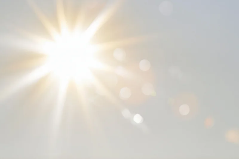 Intense sun flare bursting from center-left against a bright sky with soft bokeh highlights and copyspace
