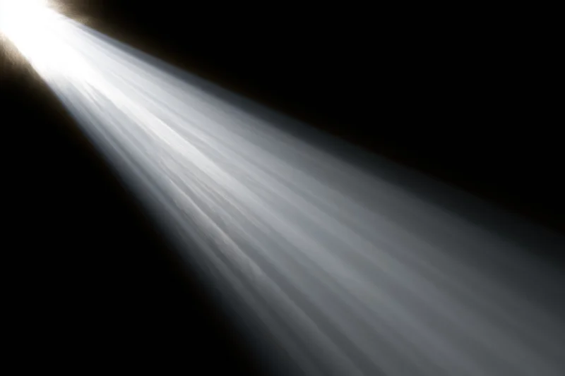 Intense white light rays radiating diagonally from upper left across dark background