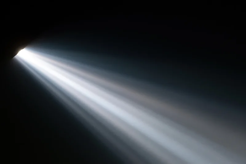Intense white light rays radiating diagonally from upper-left corner into dark space
