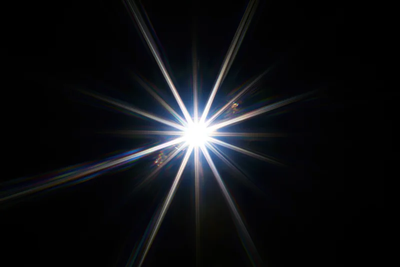 Intense white starburst lens flare centered against a pure black background