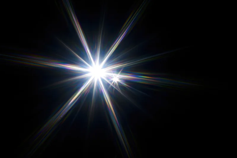 Intense white starburst lens flare centered against a pure black background