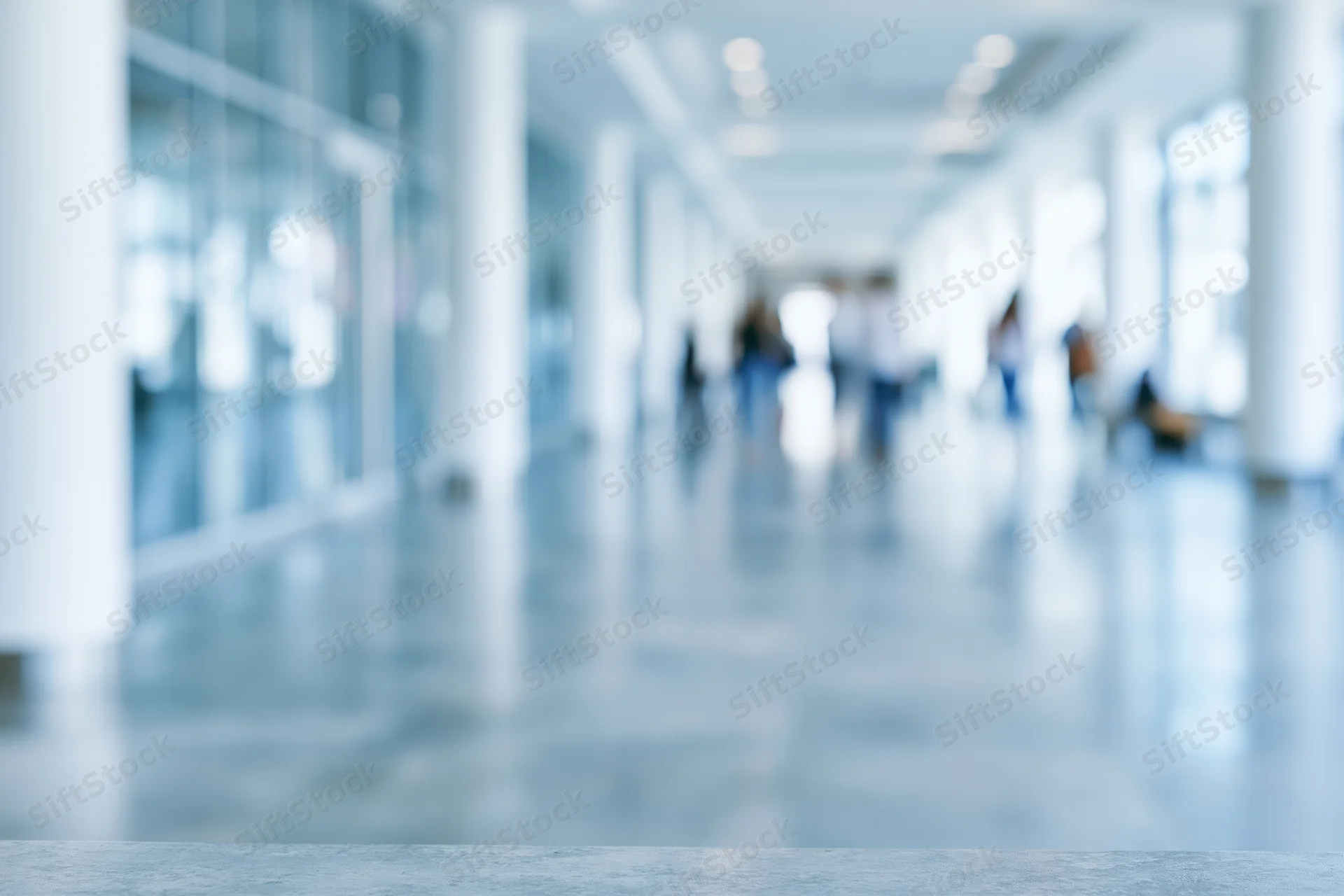 Defocused modern office corridor with blurred people walking inside, glass partitions and white columns along polished floor