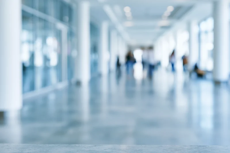 Defocused modern office corridor with blurred people walking inside, glass partitions and white columns along polished floor