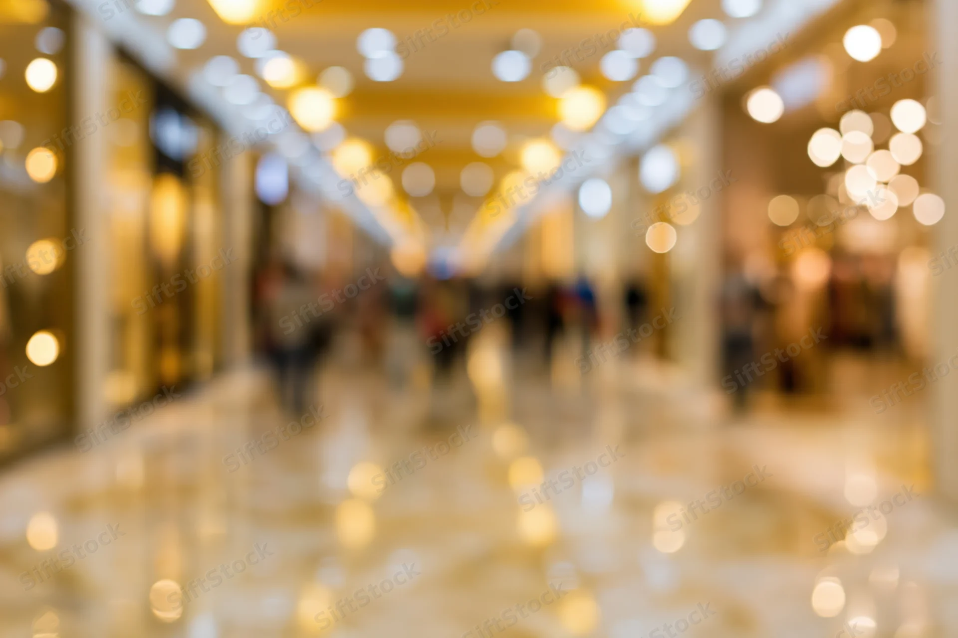 Defocused interior of an upscale shopping mall with bokeh lights and people walking along a marble corridor