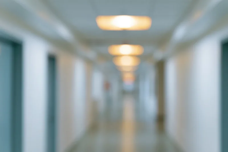 Defocused view down a long empty hospital corridor with ceiling lights and doors on either side