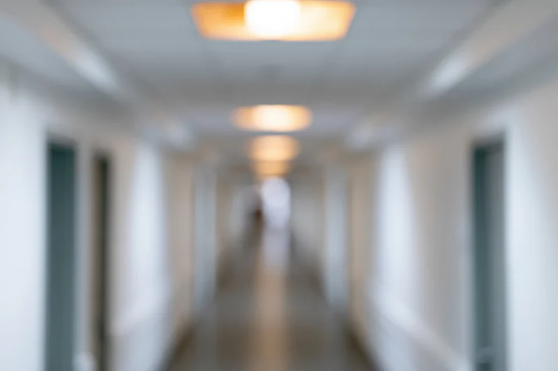 Defocused view down a long empty hospital hallway with doors and ceiling lights