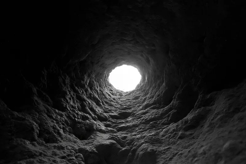 Hand-carved rock tunnel receding toward a bright circular opening at the end