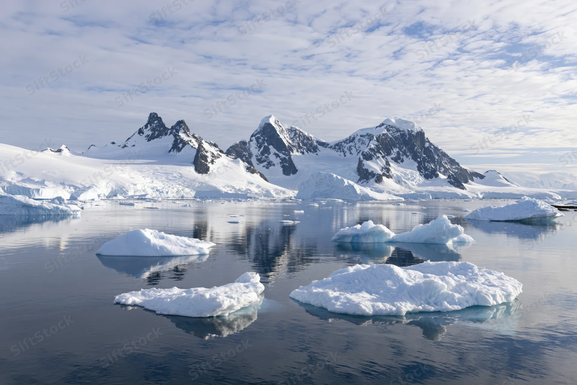 Jagged snow-covered mountain peaks rising above calm icy waters in antarctica