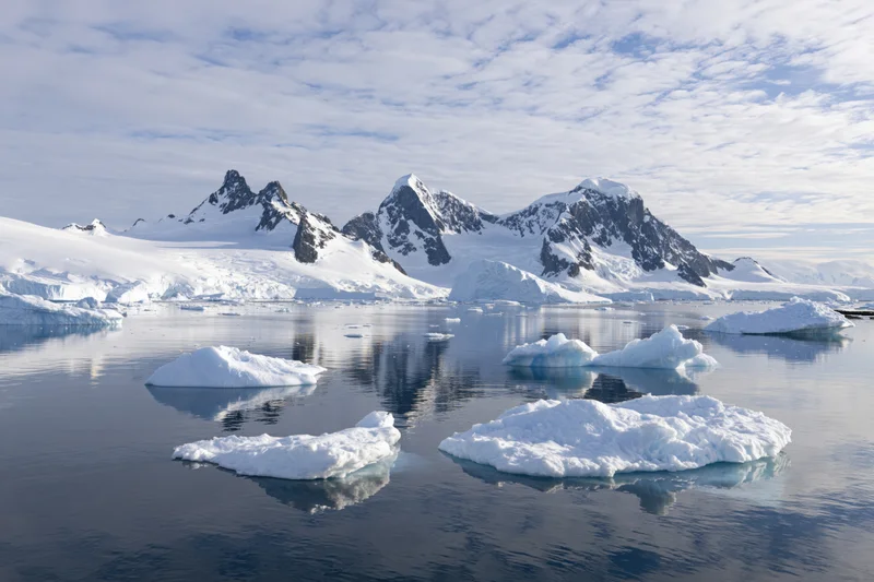 Jagged snow-covered mountain peaks rising above calm icy waters in antarctica