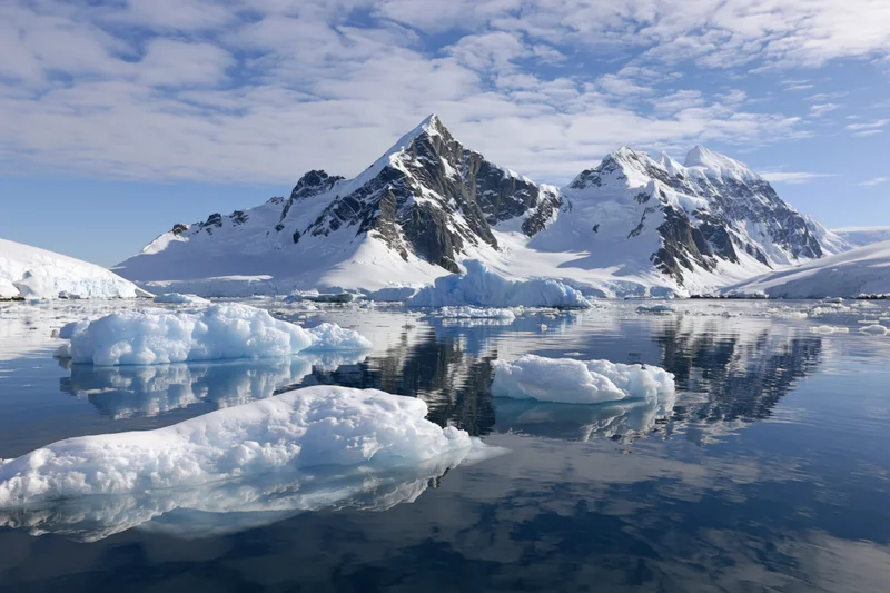 Jagged snow-covered mountain peaks rising above calm icy waters in antarctica
