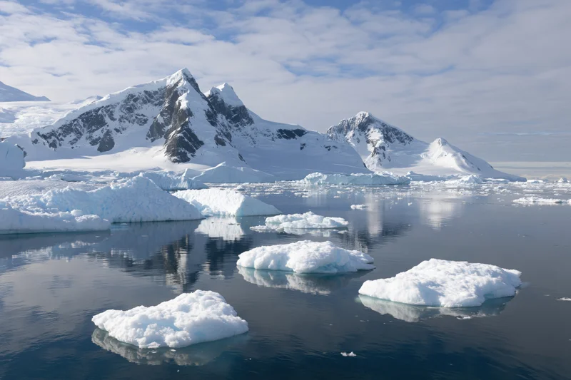 Jagged snow-covered mountain peaks rising above icy ocean with floating icebergs in antarctica