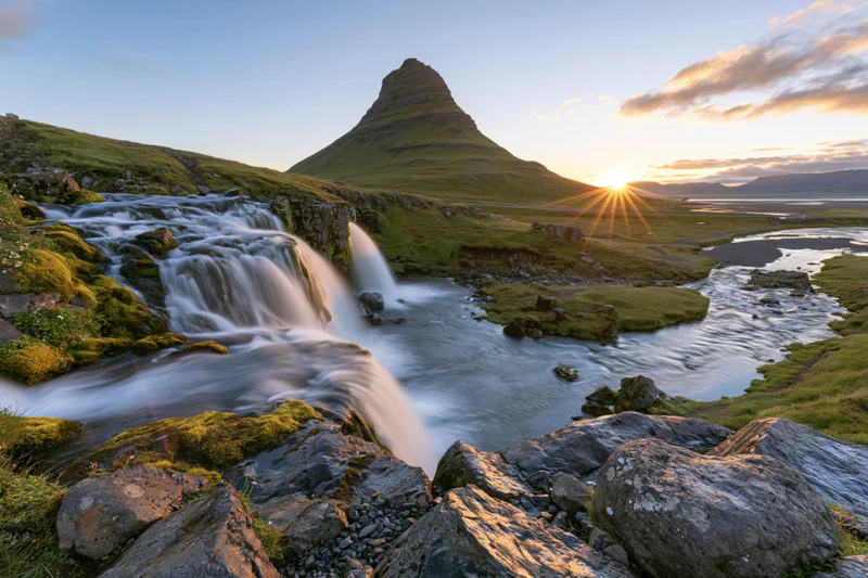 Kirkjufell mountain rising behind cascading waterfall in a mossy valley at sunset