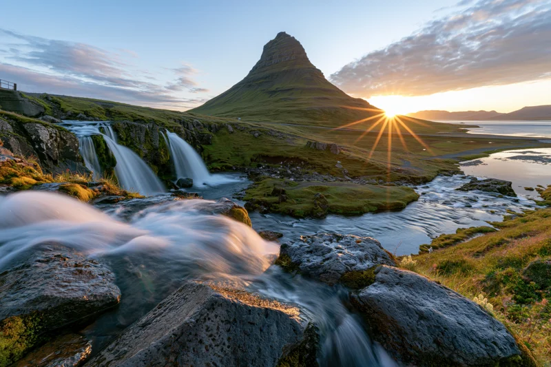 Kirkjufell mountain rising behind cascading waterfall at sunset near coastal grassland