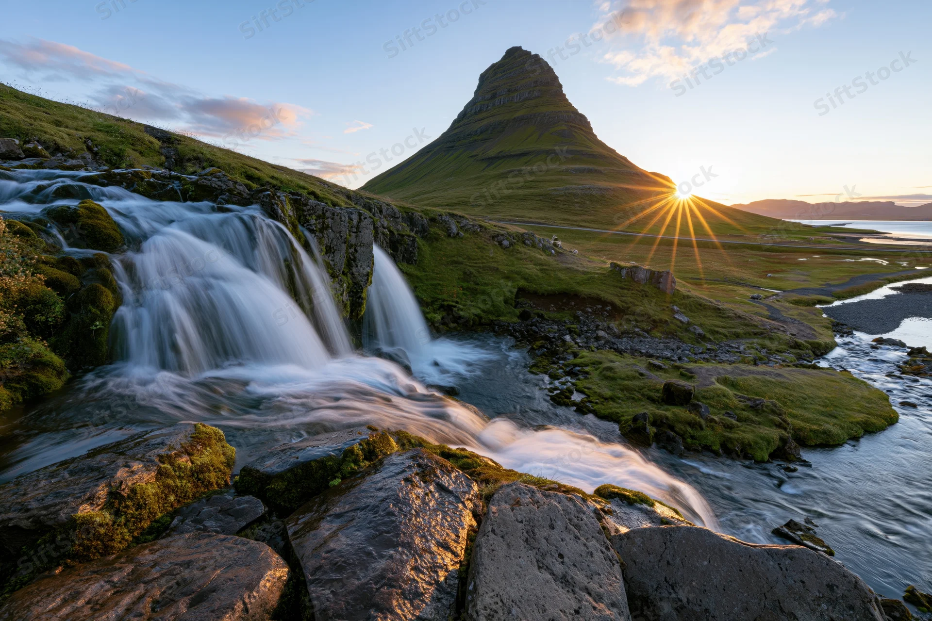 Kirkjufell mountain rising behind cascading waterfall in icelandic landscape at sunset