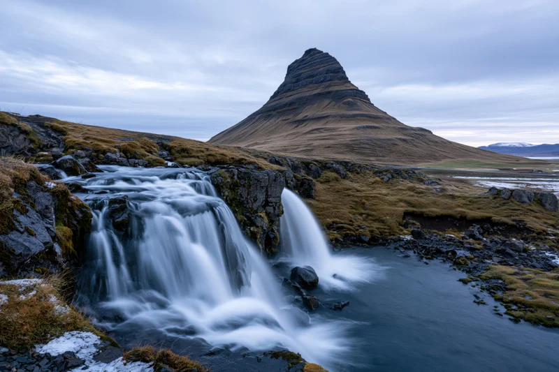 Kirkjufell mountain rising sharply above a cascading waterfall in icelandic landscape