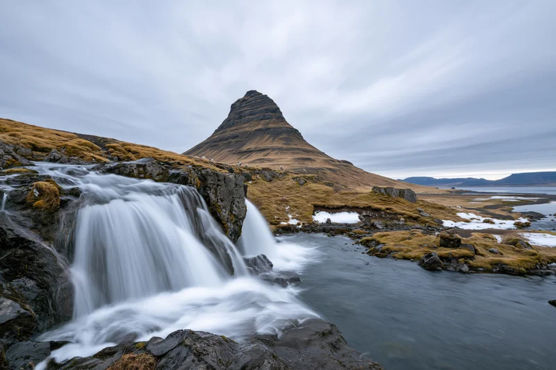 Kirkjufell mountain rising sharply above a cascading waterfall and mossy coastal terrain in iceland