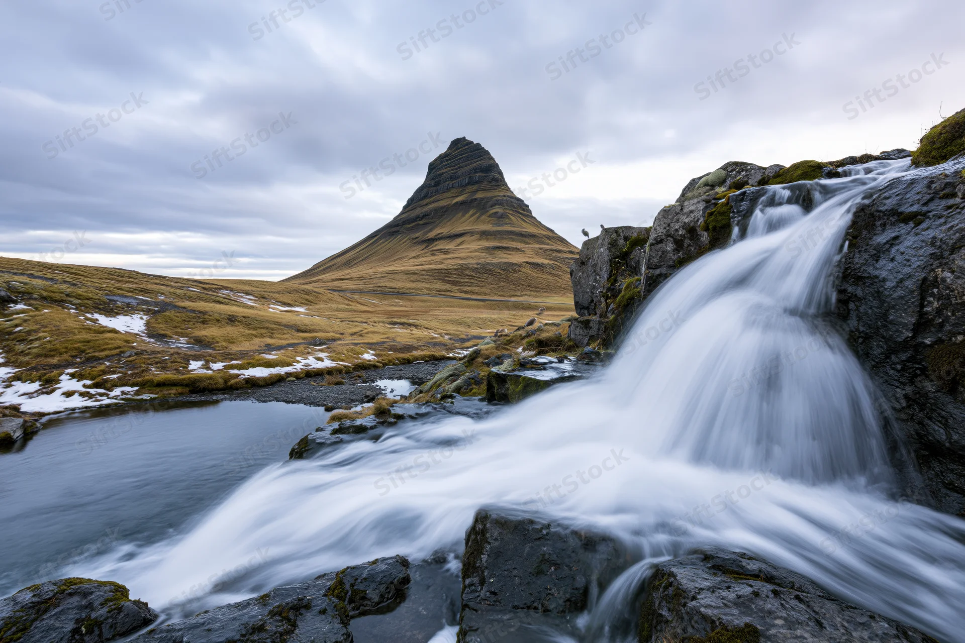 Kirkjufell mountain rising sharply above a flowing waterfall in icelandic tundra landscape