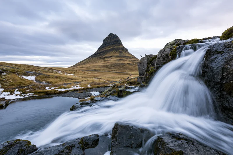 Kirkjufell mountain rising sharply above a flowing waterfall in icelandic tundra landscape