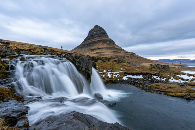 Kirkjufell mountain rising sharply above a cascading waterfall in icelandic tundra landscape
