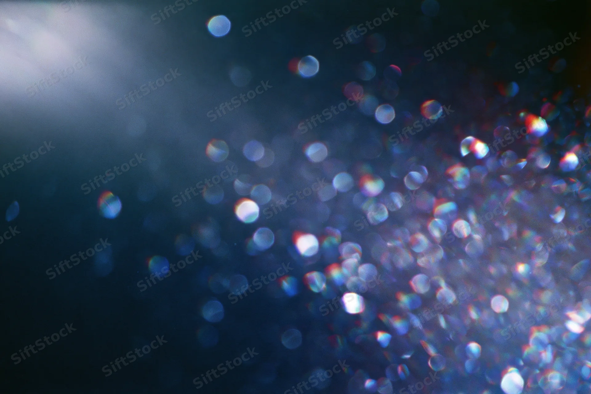 Abstract bokeh lights glowing in dark background with lens flare and iridescent sparkle