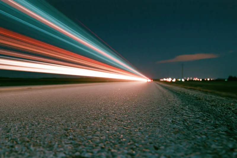 Long-exposure light trails from vehicles moving along a dark asphalt road at night