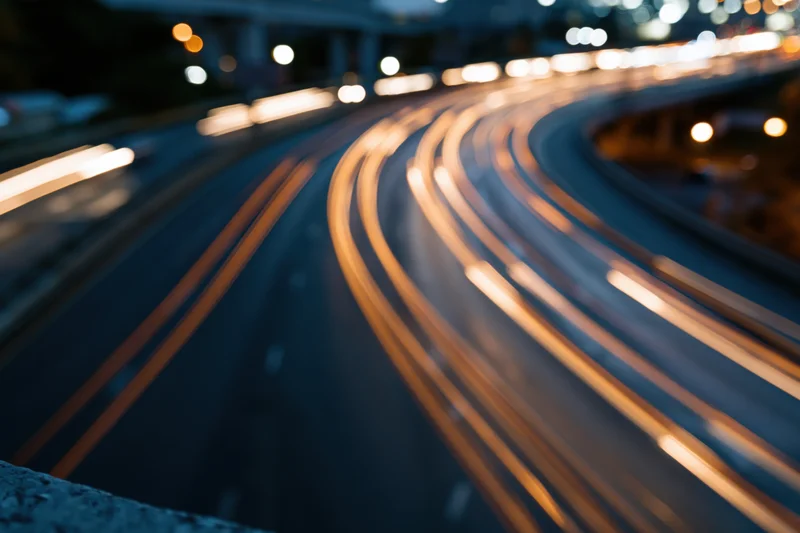 Curved urban highway at night with light trails from moving vehicles