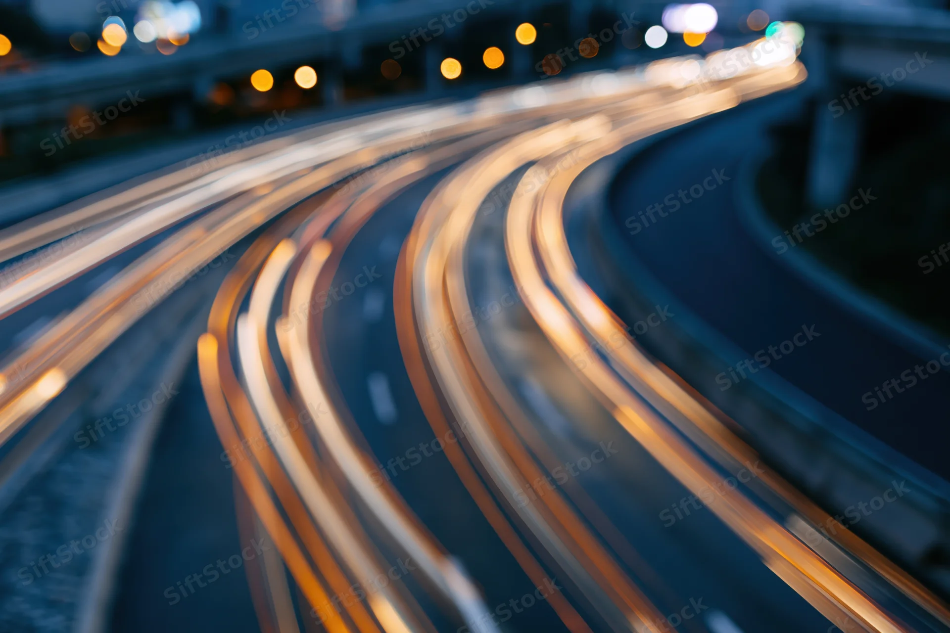 Curved urban highway at night with light trails from moving vehicles