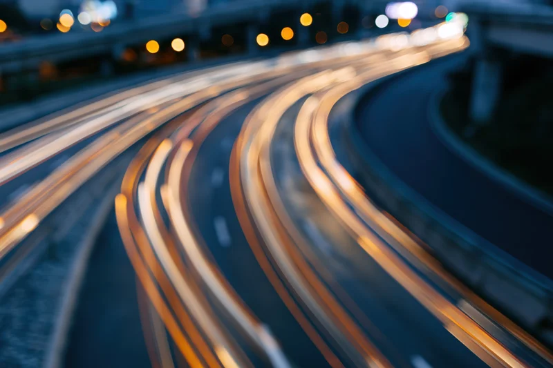 Curved urban highway at night with light trails from moving vehicles