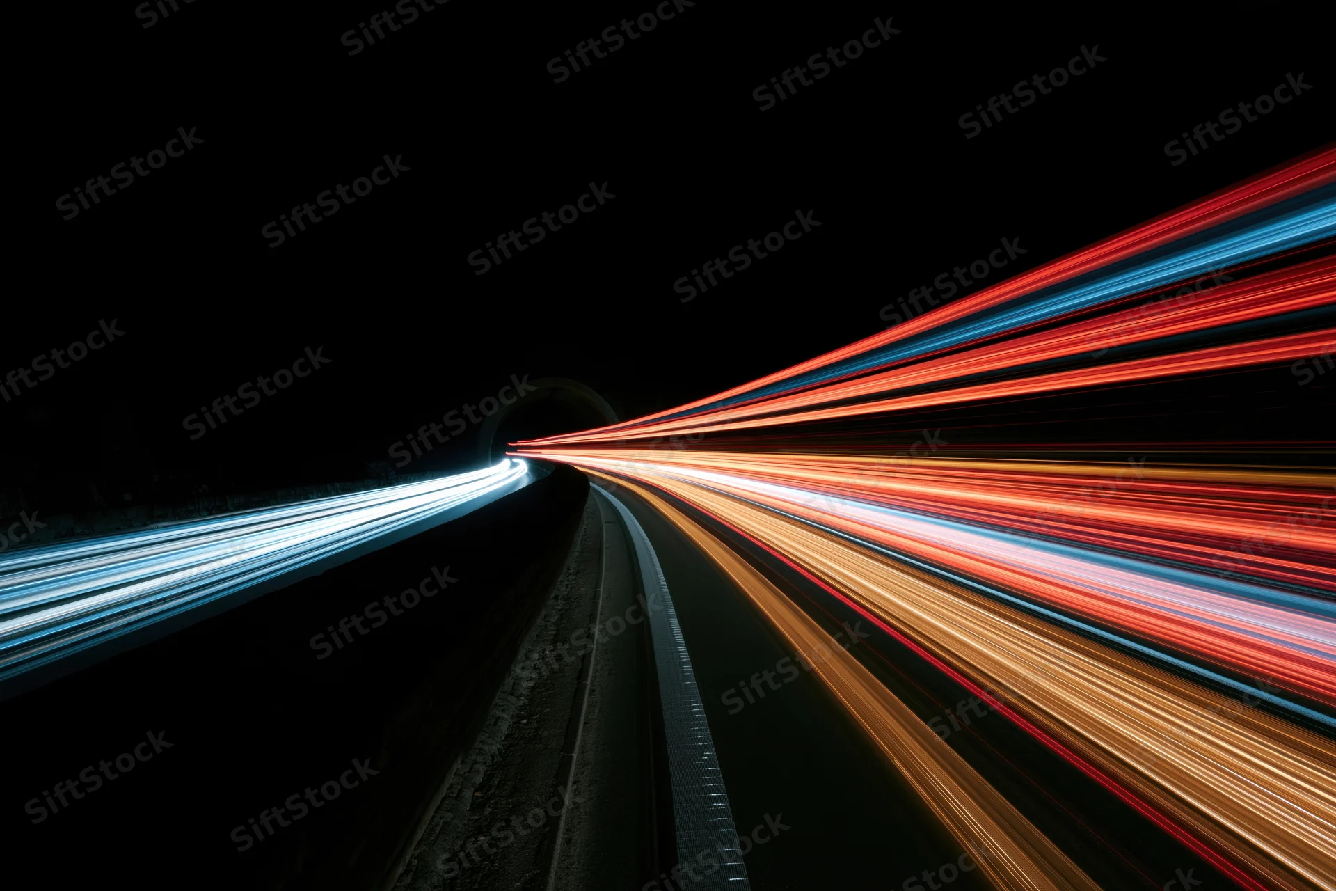 Long-exposure night view of curving highway with light trails from moving vehicles entering tunnel