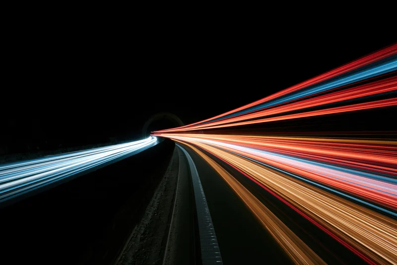 Long-exposure night view of curving highway with light trails from moving vehicles entering tunnel