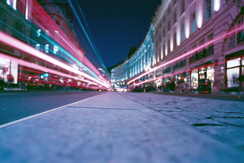 Long-exposure night view of a curved london street with light streaks from moving traffic along illuminated storefronts