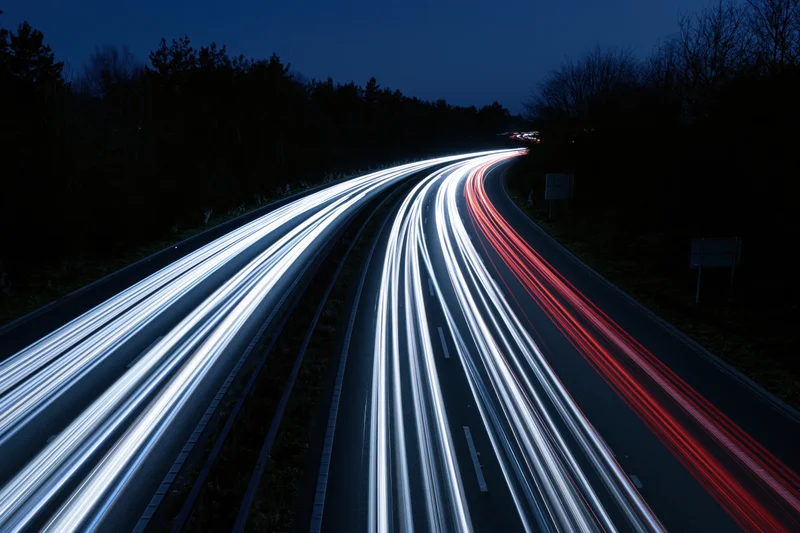 Long-exposure night view of curved dual-carriageway highway with light trails from moving vehicles