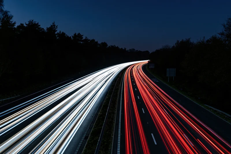 Curved dual-carriageway highway at night with long-exposure light trails from moving vehicles