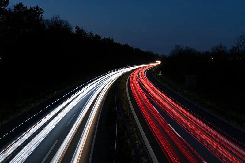 Long-exposure night view of curved dual-carriageway highway with light trails from moving vehicles