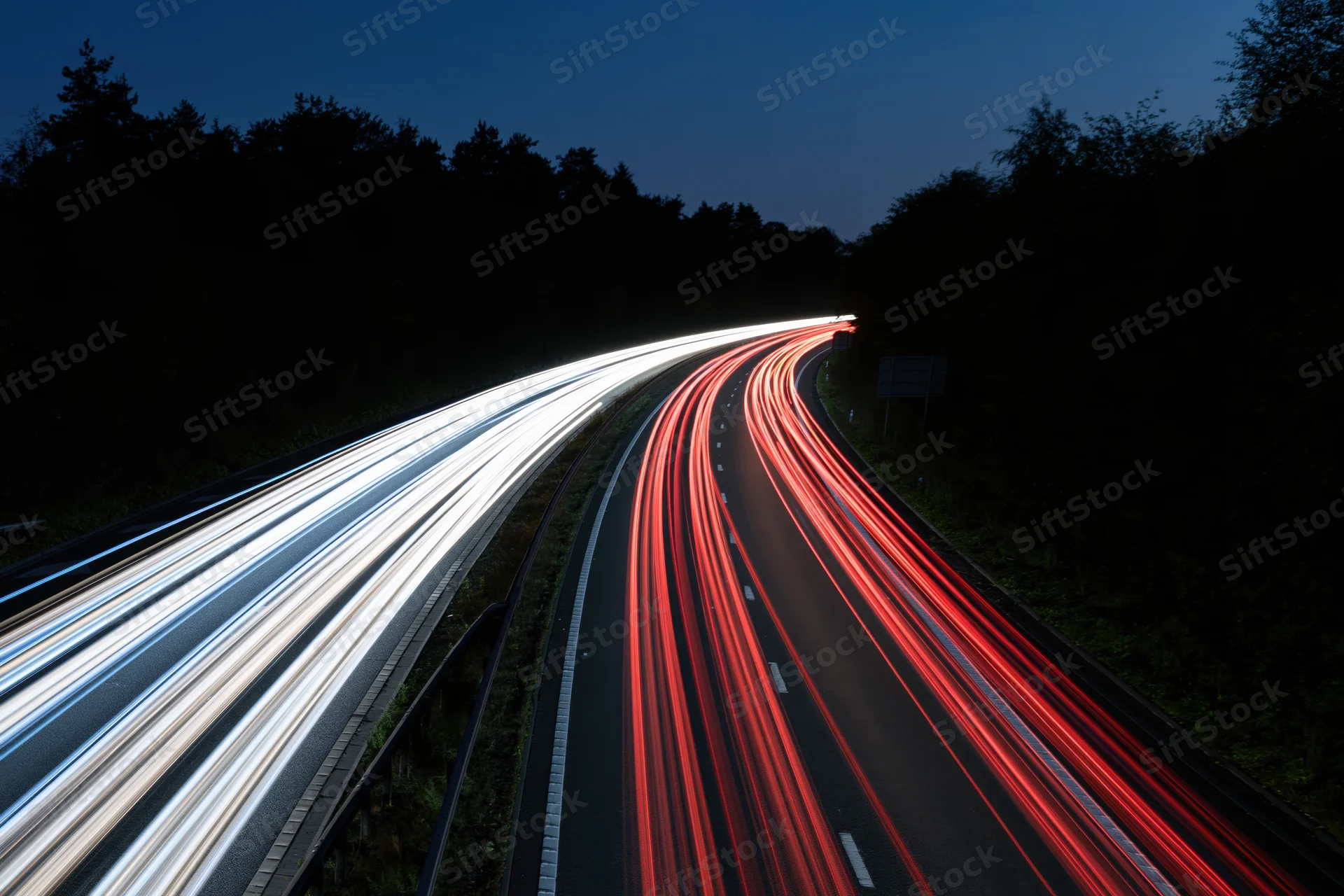 Long-exposure night view of curved dual-carriageway highway with light trails from moving vehicles
