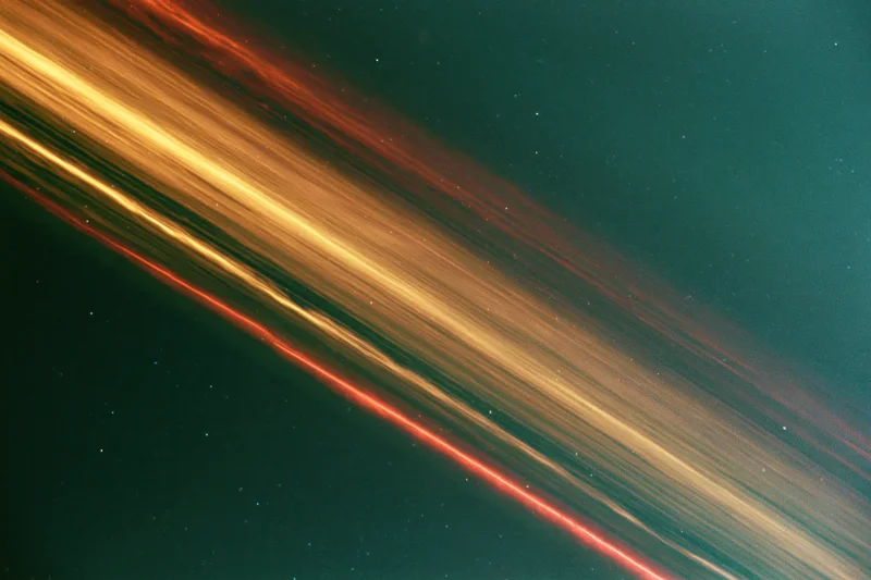 Long-exposure night sky photograph showing sweeping light streaks across dark teal background with scattered stars