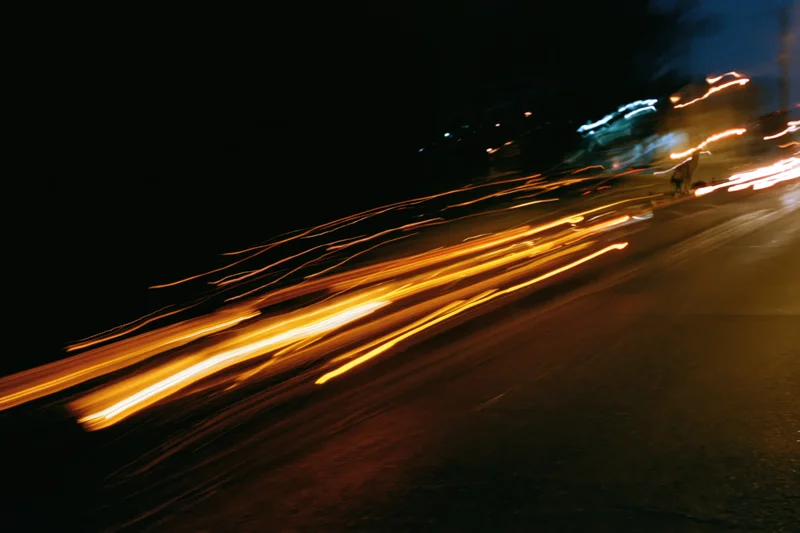 Long-exposure night street scene with light trails from moving vehicles on a dark urban road