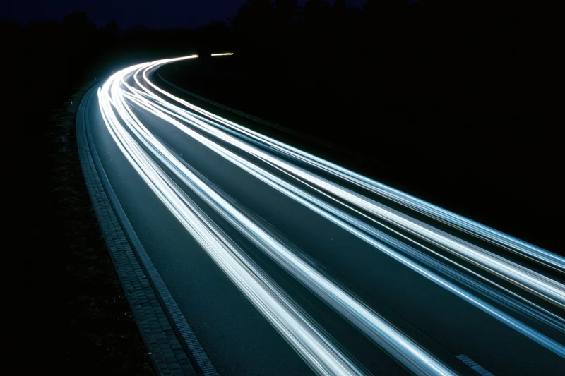 Long-exposure light trails from vehicles moving along a curved highway at night
