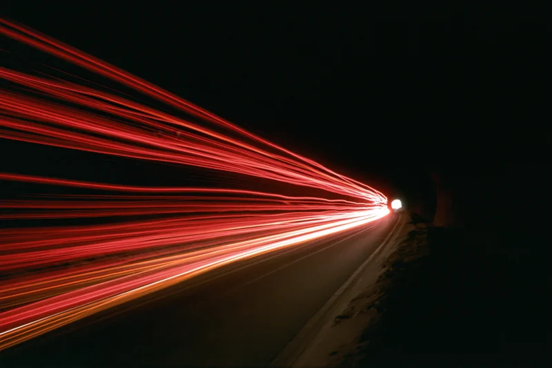 Red light trails from vehicles curving through a dark tunnel at night