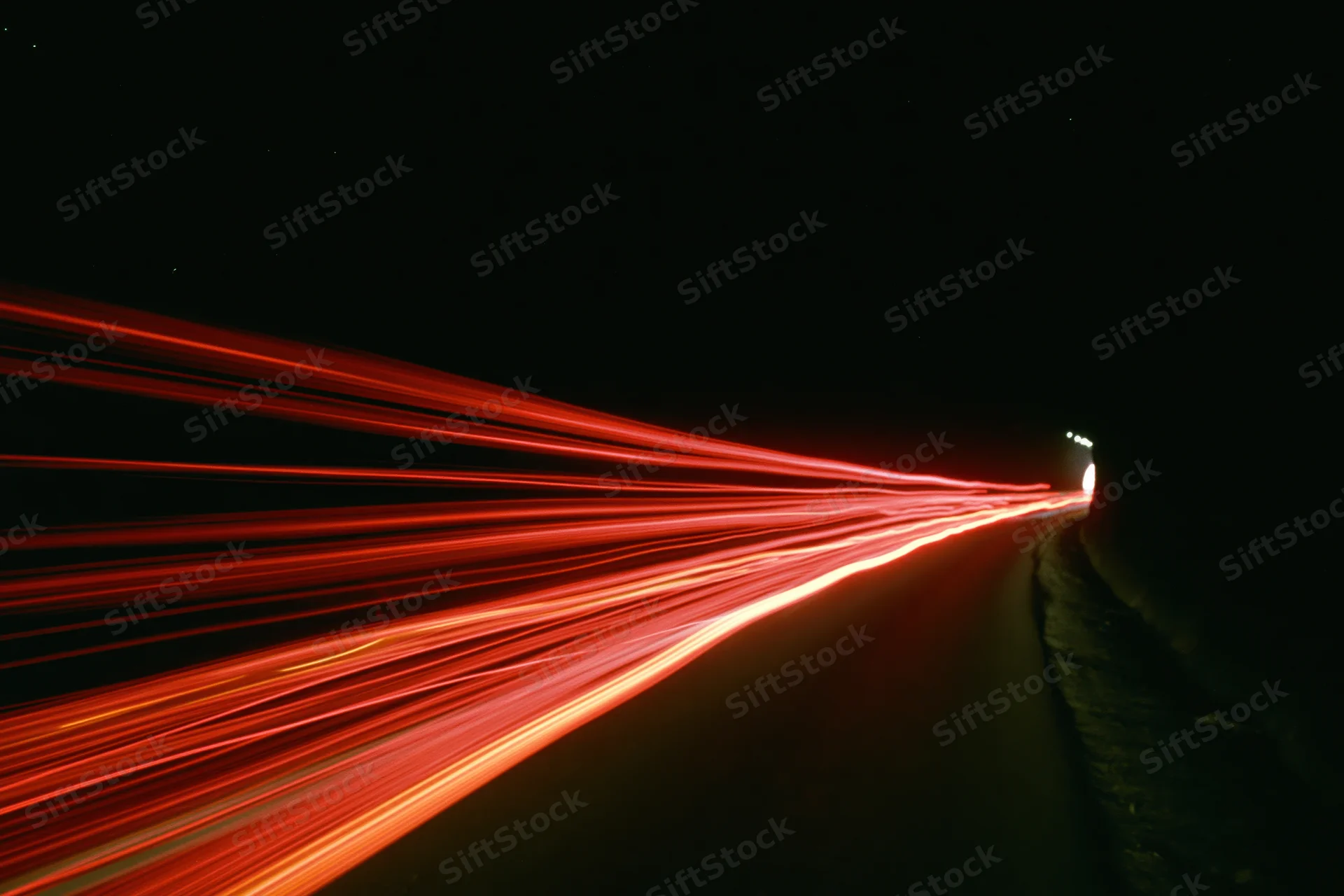 Red light trails from moving vehicles curving along a dark highway at night