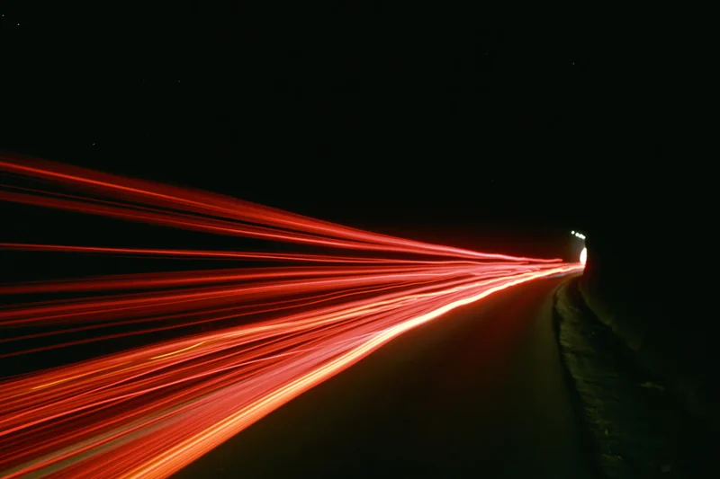 Red light trails from moving vehicles curving along a dark highway at night