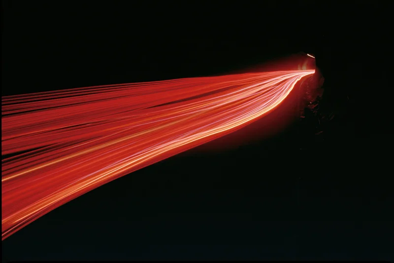 Red car light trails curving along a dark road at night