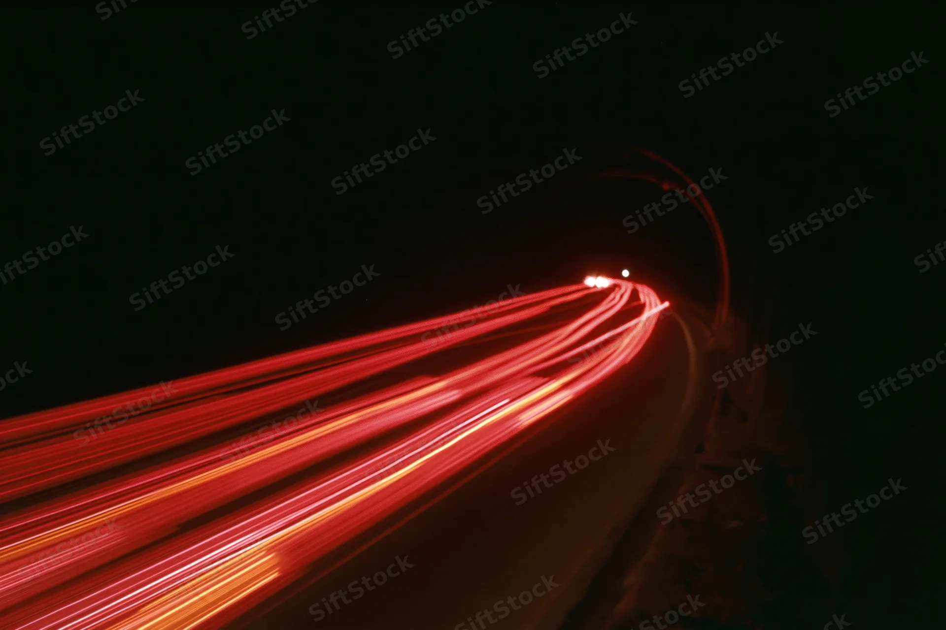 Red light trails from vehicles moving along a curving road at night