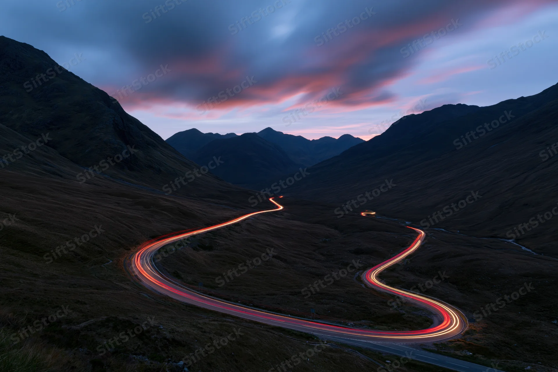 Winding mountain road with light trails from vehicles at twilight