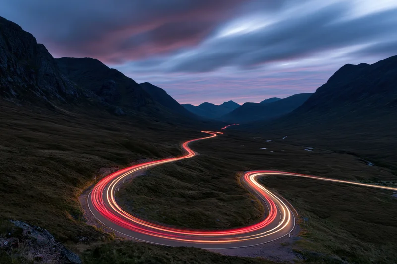 Winding mountain road with light trails from vehicles at twilight in a valley