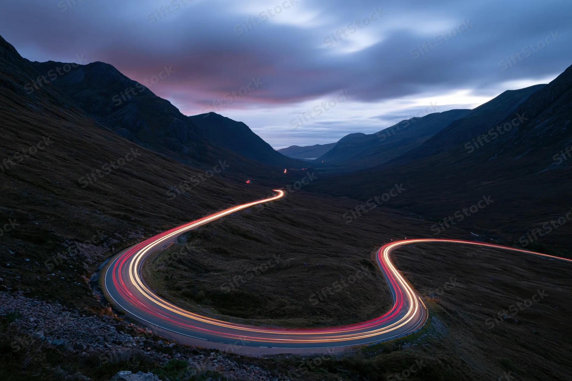 Winding mountain road with light trails from vehicles at twilight in a valley