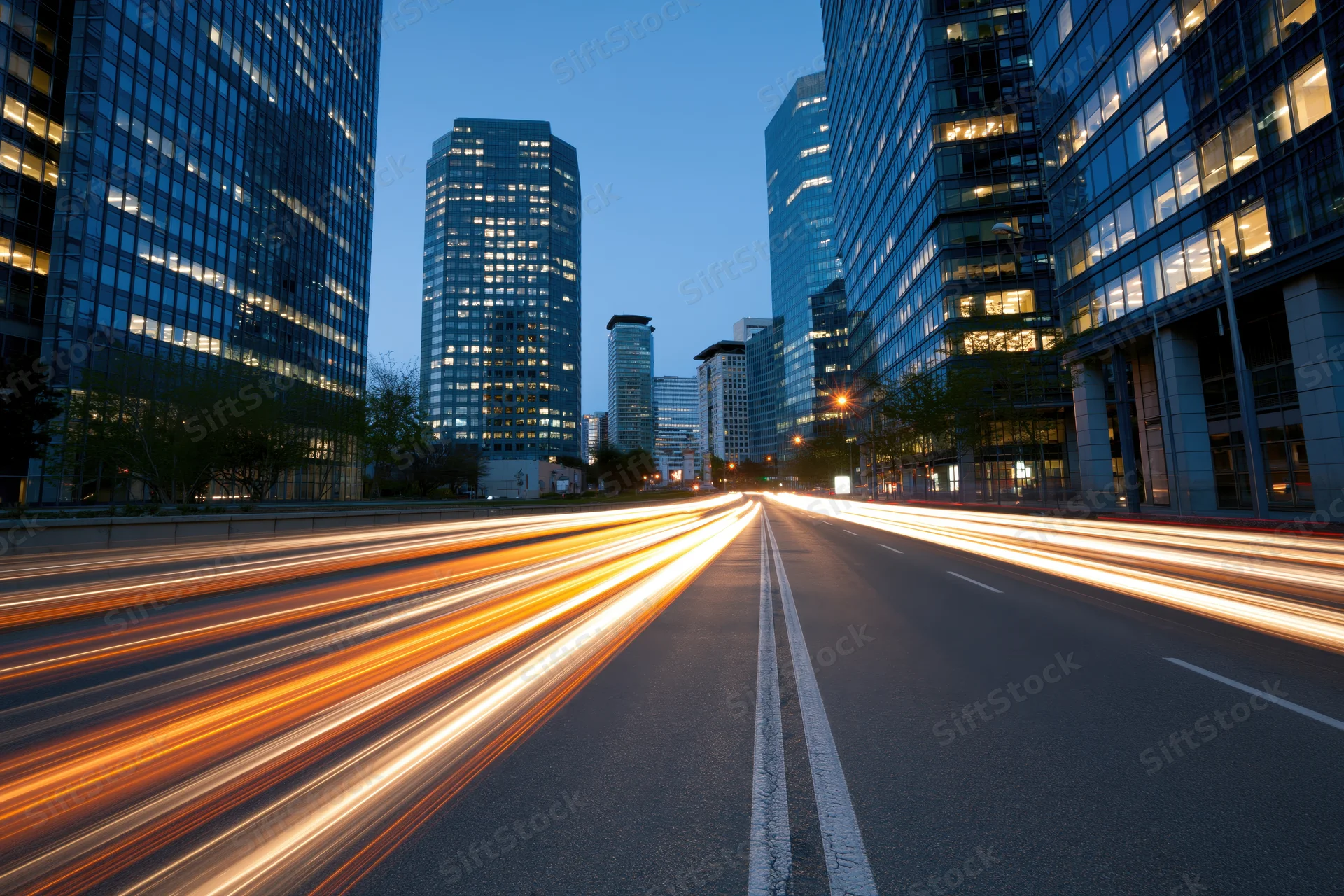 Light trails from moving vehicles on a city highway at dusk surrounded by tall glass office buildings