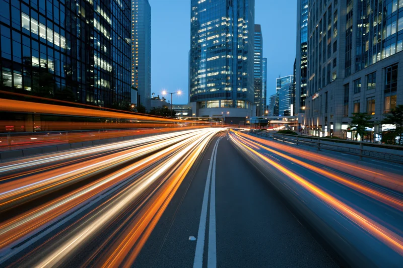 Light trails from moving vehicles on a city highway at dusk surrounded by illuminated skyscrapers